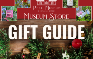 Rustic wooden background with christmas garland at the bottom (decorated with dried oranges and cranberries). The words "Peel Museum & Botanical Garden Museum Store Gift Guide" in white on a red ribbon next to photos of gifts (dragonfly ornament, jam, bath bombs, chocolate bar)