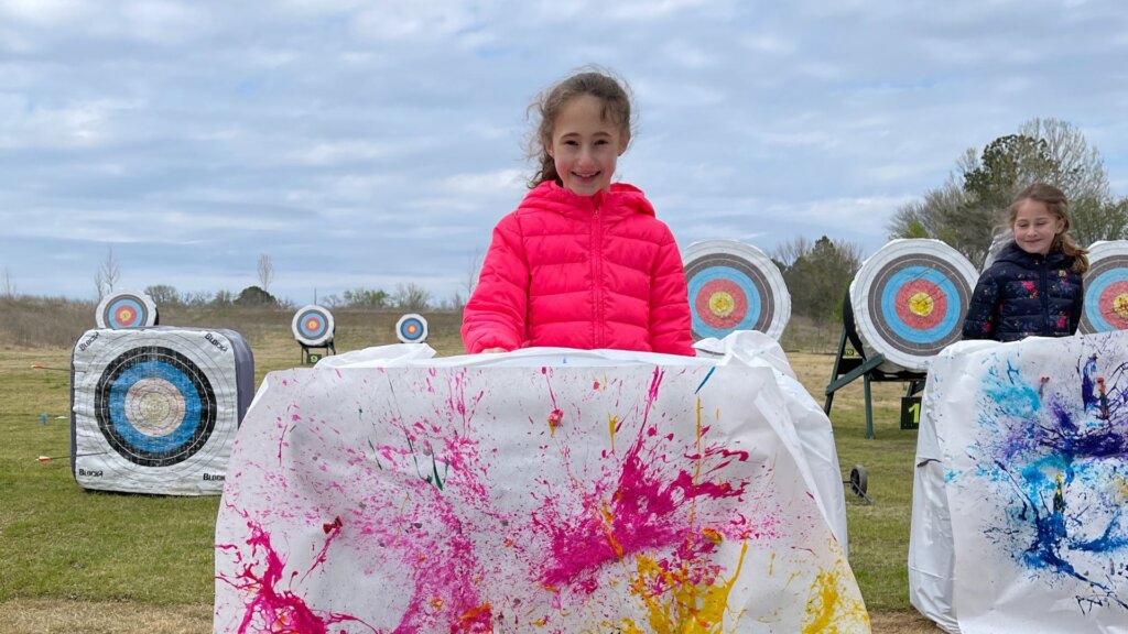 Young child standing behind paint splatter art with blue skies in the background in Bentonville, AR